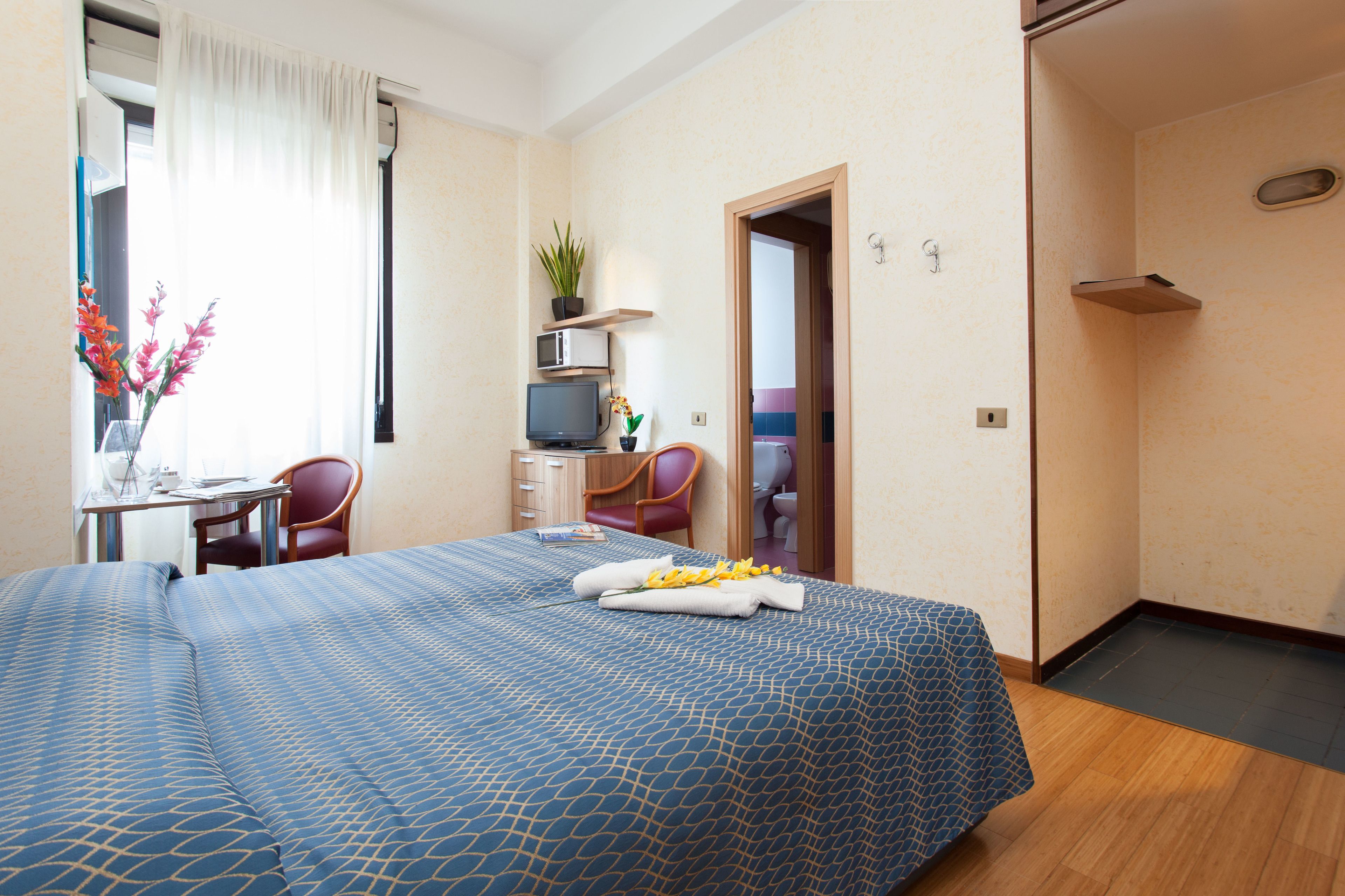 Una habitación de hotel con cama, escritorio, silla, televisión y puerta del baño.