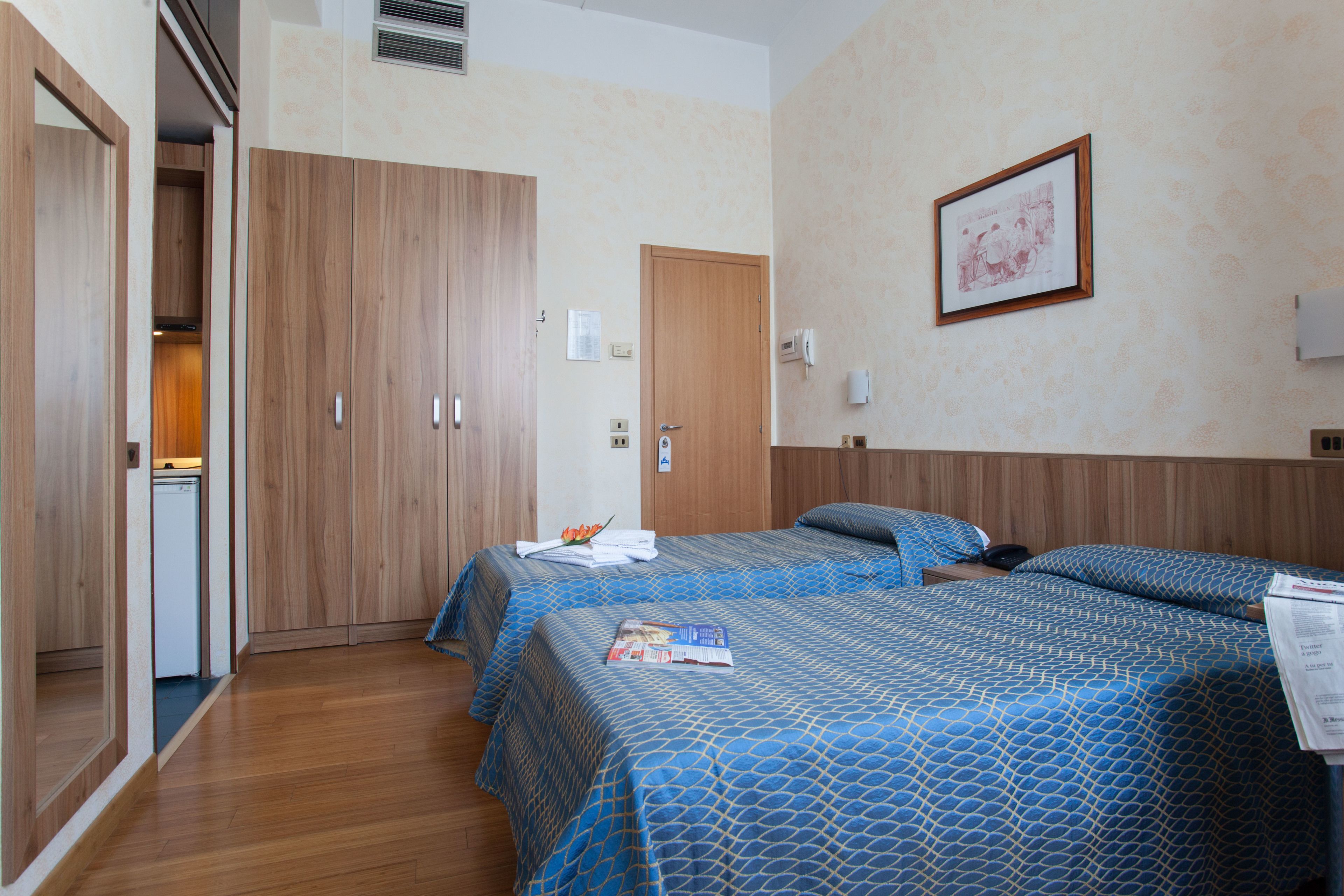Ein Hotelzimmer mit zwei Betten, Holzschränken, einer kleinen Küchenzeile und einem gerahmten Bild an der Wand.