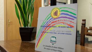 Un cartel con texto en italiano e inglés, sobre una mesa de madera con una planta en maceta al lado.