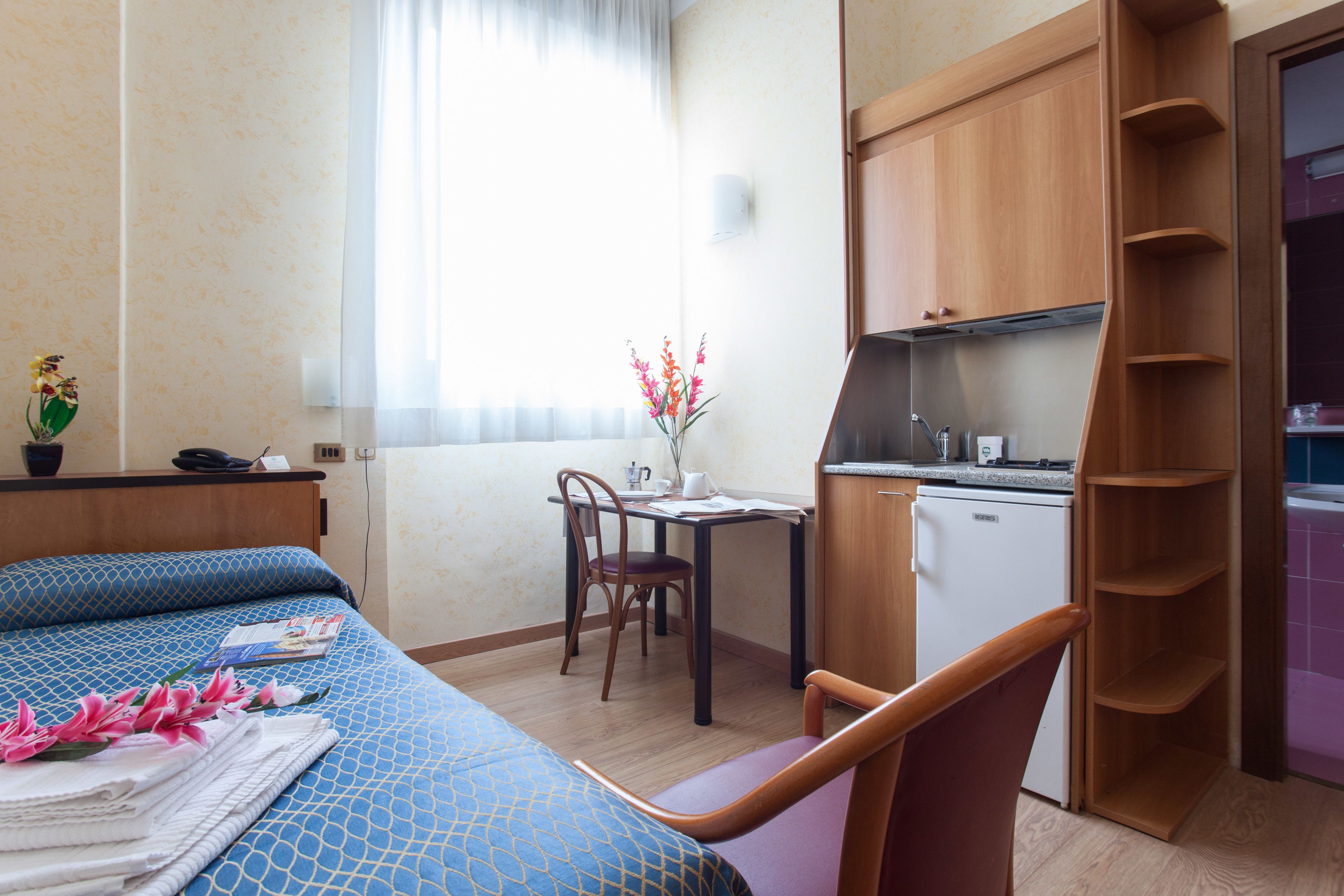 Une chambre d’hôtel équipée d’un lit, d’un bureau, d’une chaise, d’une petite kitchenette et d’une fenêtre avec des rideaux.