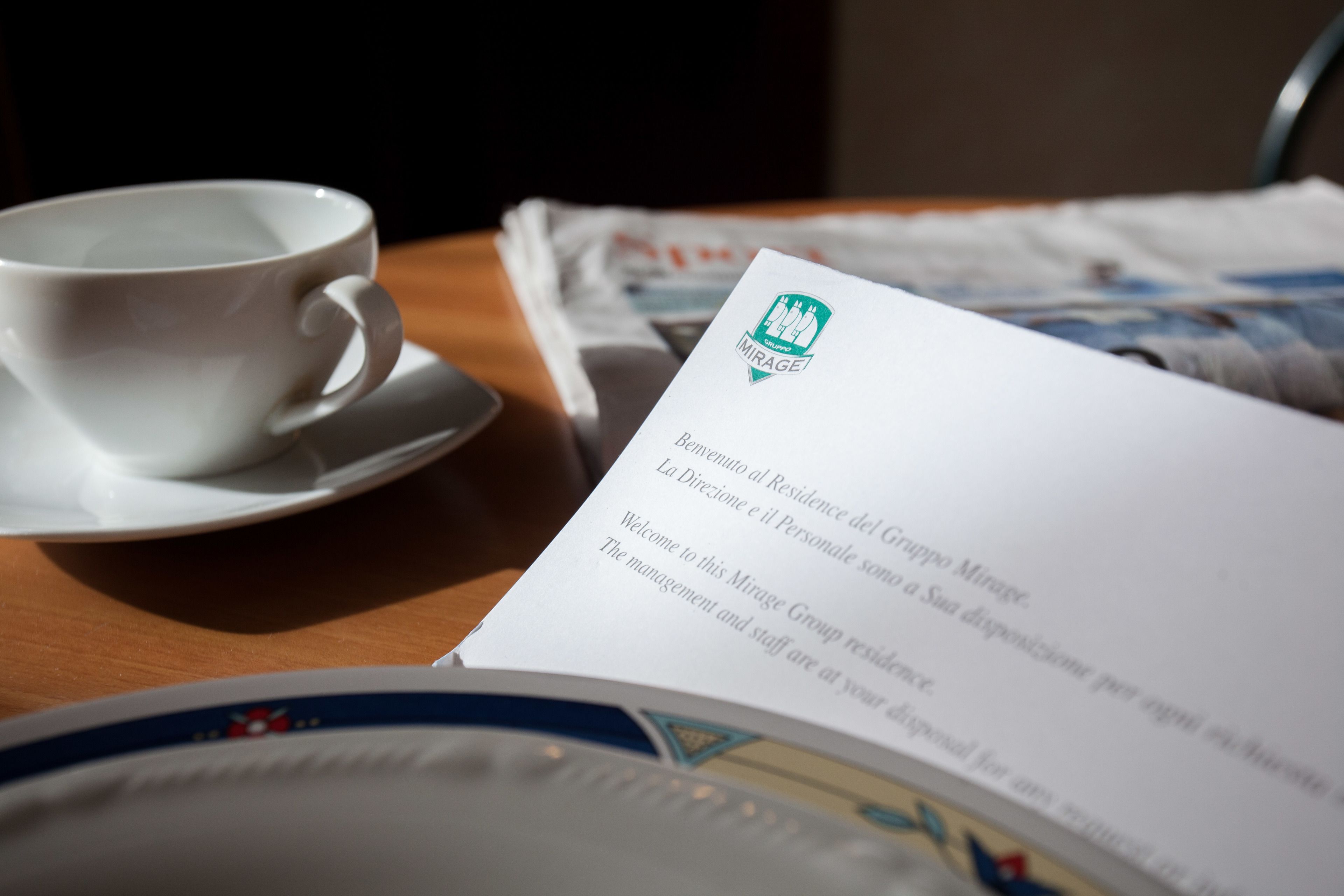 Une tasse de café posée sur une soucoupe, un menu et une assiette ornée de motifs floraux.