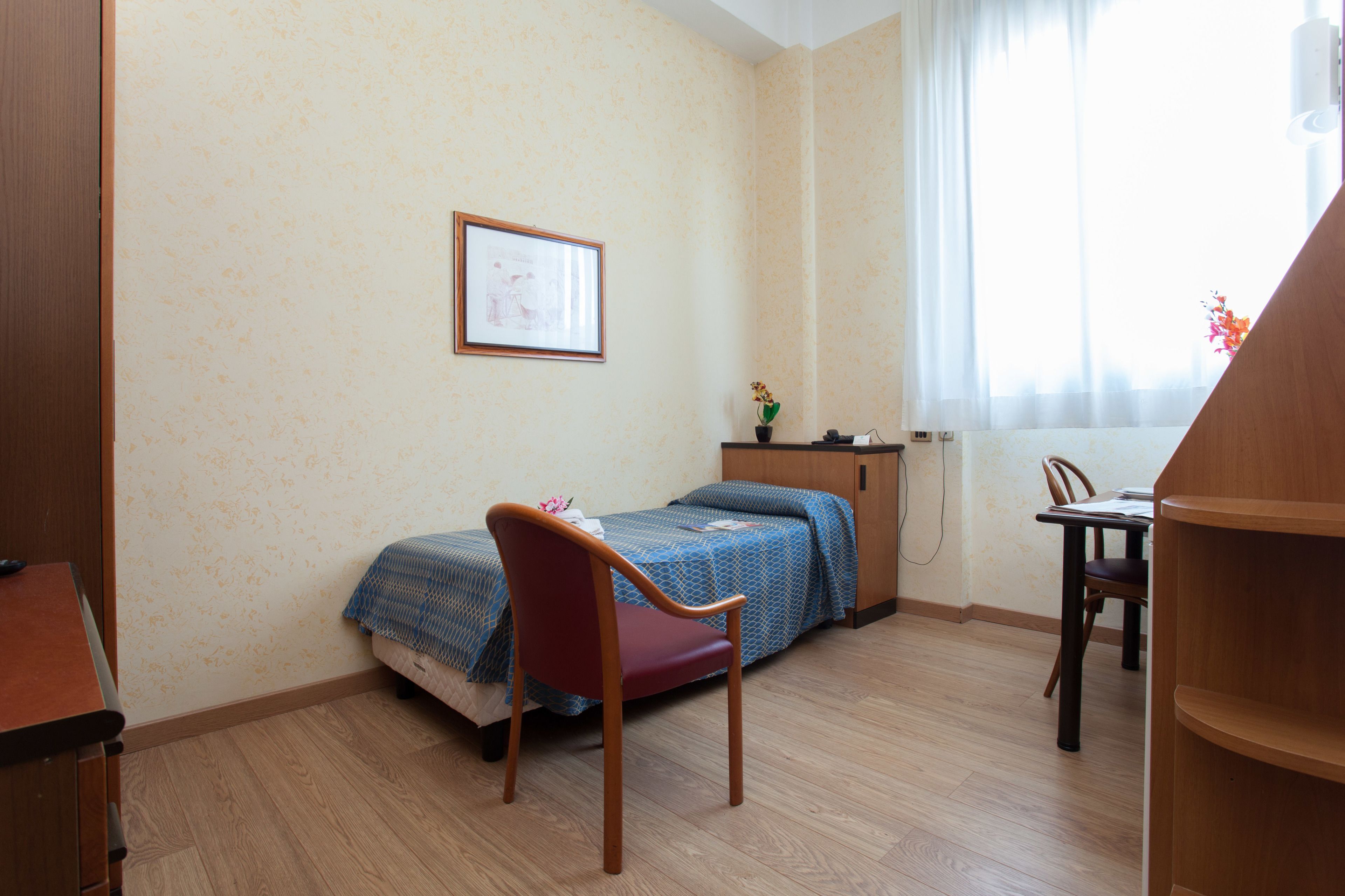 Una stanza con un letto, una scrivania, una sedia e una finestra con tende.