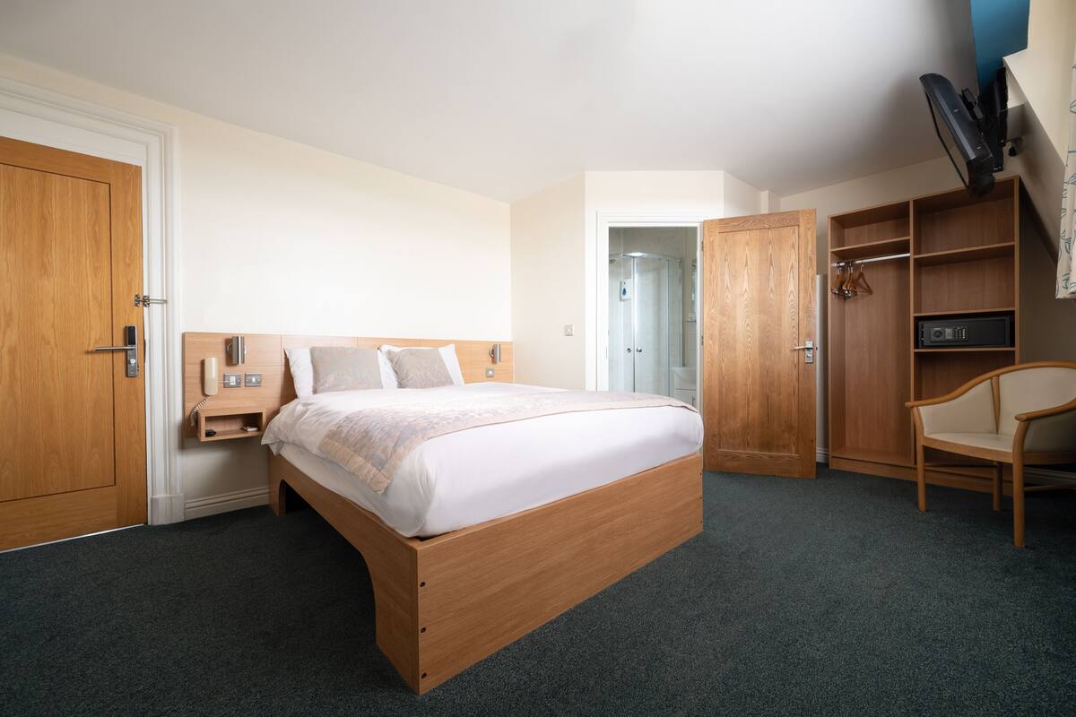 A hotel room with a wooden bed, a wardrobe, a chair, and a TV mounted on the wall.