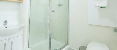 Un baño con ducha acristalada, lavamanos, inodoro y toallero.
