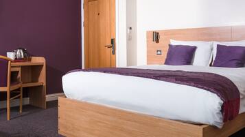 A single bed with a wooden frame, a wooden nightstand with a kettle and cup, and a door with a wooden frame.