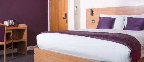A single bed with a wooden frame, a wooden nightstand with a kettle and cup, and a door with a wooden frame.