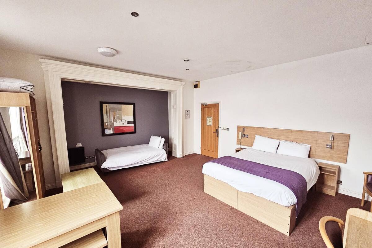 A hotel room with a large bed, a desk, and a chair.