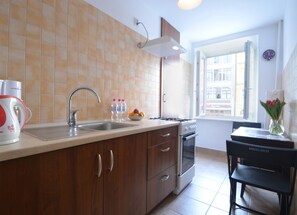 Une cuisine équipée d’un évier, d’une cuisinière et de placards. On y trouve deux bouteilles d’eau et un saladier rempli de fruits sur le comptoir.