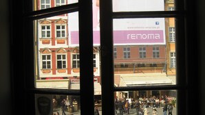 A view through a window with a sign for 'RENOMA KOCHA MODE!' and a reflection of a busy street scene. - Apartment Central (Wroclaw)