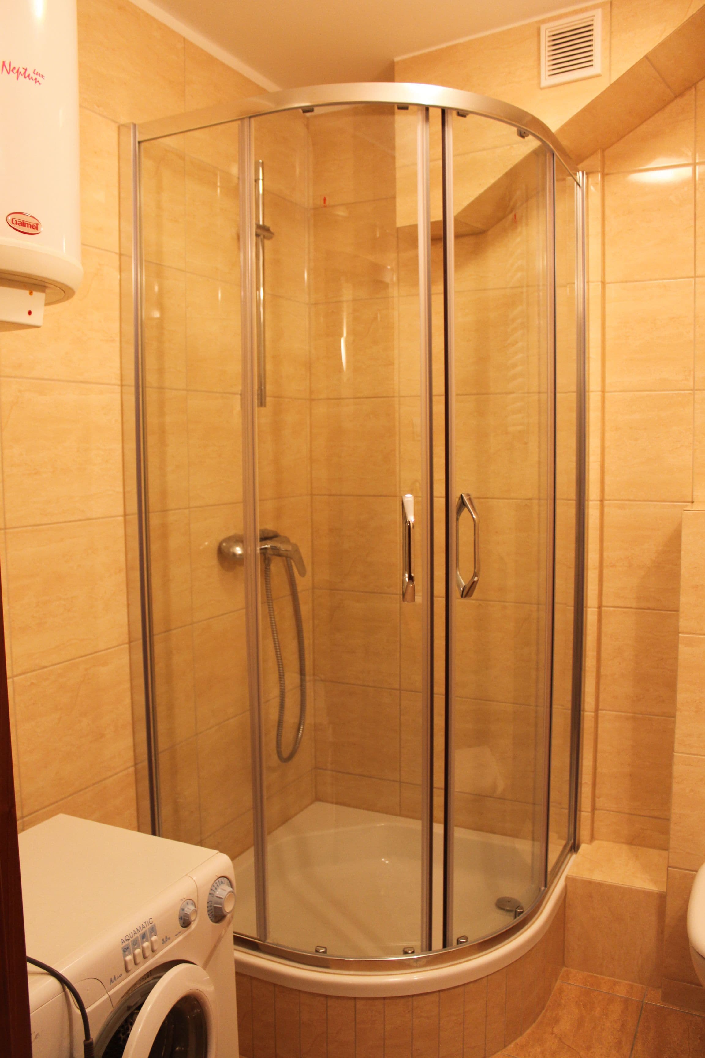 A corner shower with glass doors, a built-in toilet, and a washing machine.