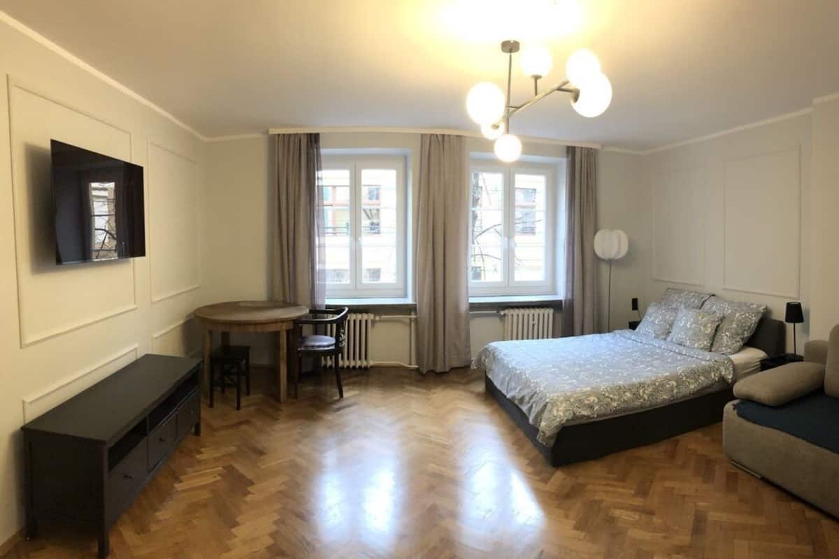 A bedroom with a bed, a desk, a chair, a TV, and a sofa.