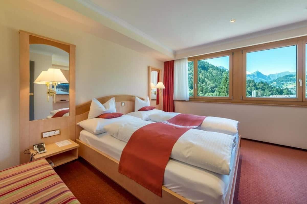 Een hotelkamer met twee bedden, een grote spiegel en uitzicht op bergen.