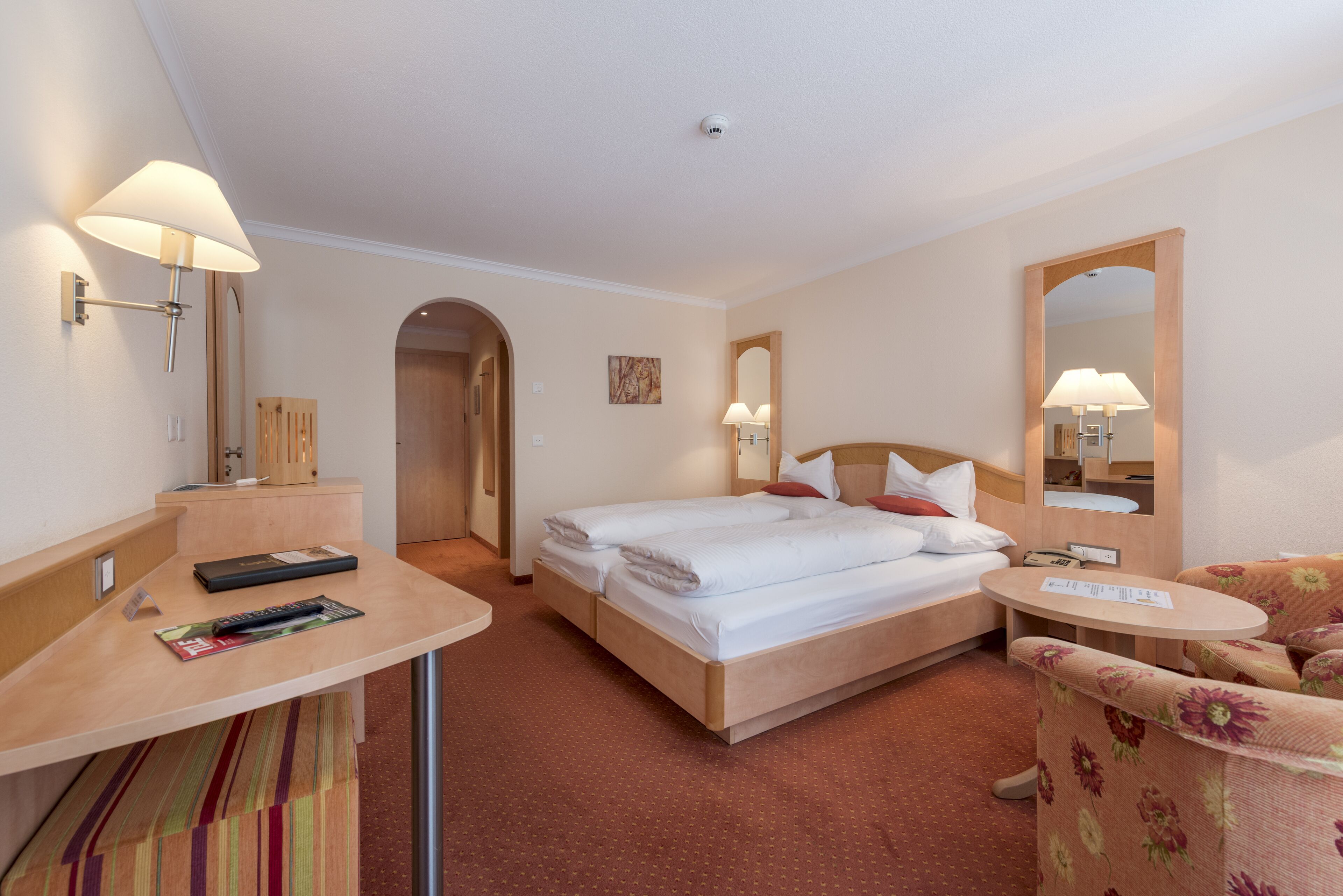 Una habitación de hotel con cama, mesita de noche, silla y espejo.