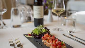 A dining table with a black slate serving board, two forks, a bottle of wine, and a glass of white wine.