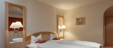 A hotel room with two beds, a round table, a mirror, and wall-mounted lamps.
