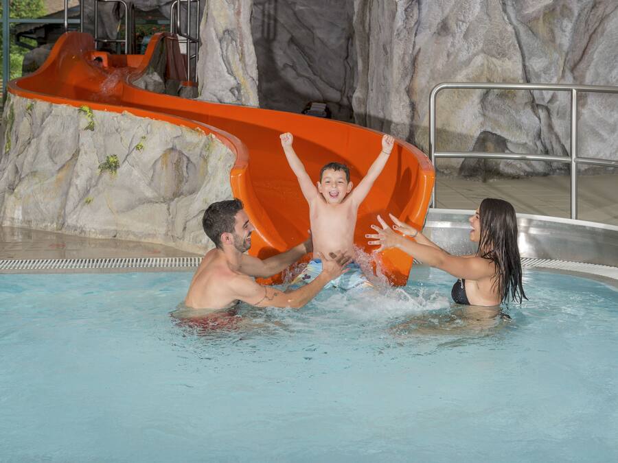 Una piscina con tobogán de agua, un puesto de socorrista y un muro rocoso de fondo.