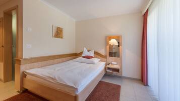 A hotel room with a bed, a bedside table, a mirror, and a window with curtains.