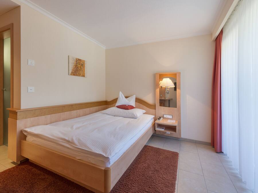 A hotel room with a bed, a bedside table, a mirror, and a window with curtains.