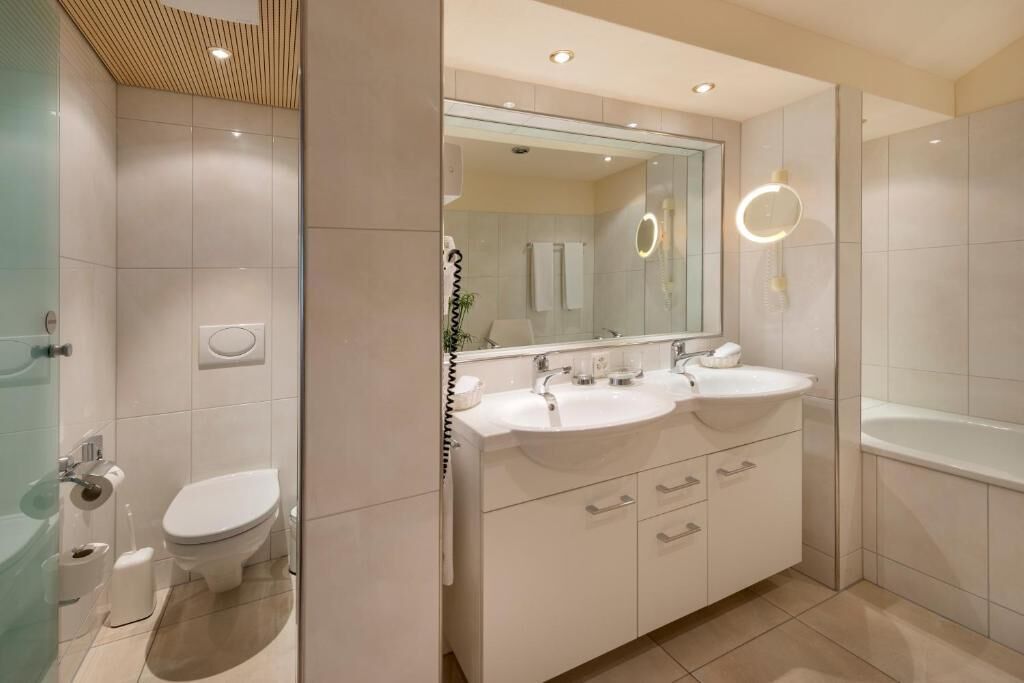 A modern bathroom with a double sink vanity, a large mirror, and a separate toilet area.