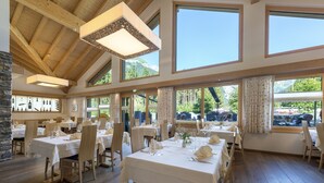 Un restaurante con varias mesas dispuestas para comer, grandes ventanales que ofrecen vistas al exterior y una estructura de techo de madera.