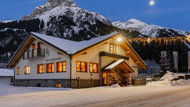 Una cabaña de montaña con letrero de restaurante, fachada de madera y alrededores nevados.