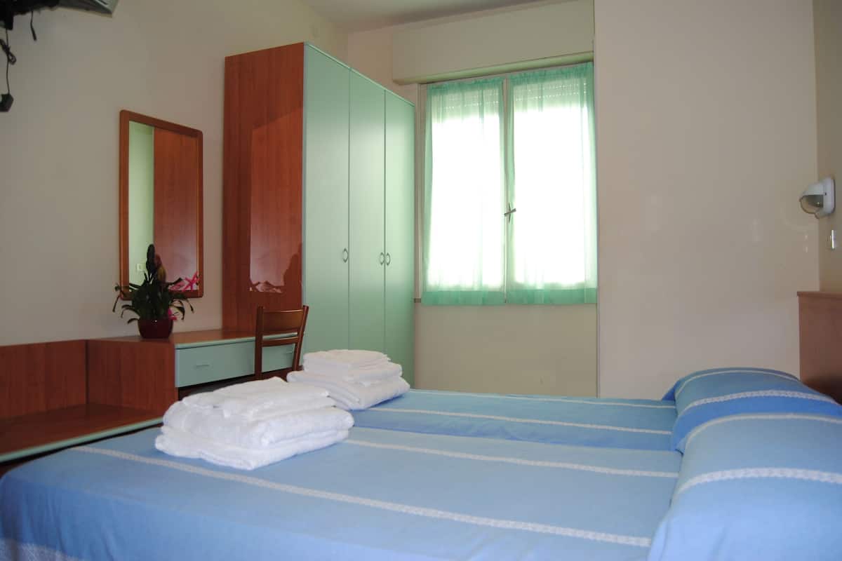 A bedroom with a bed, a wardrobe, a mirror, and a window with curtains.