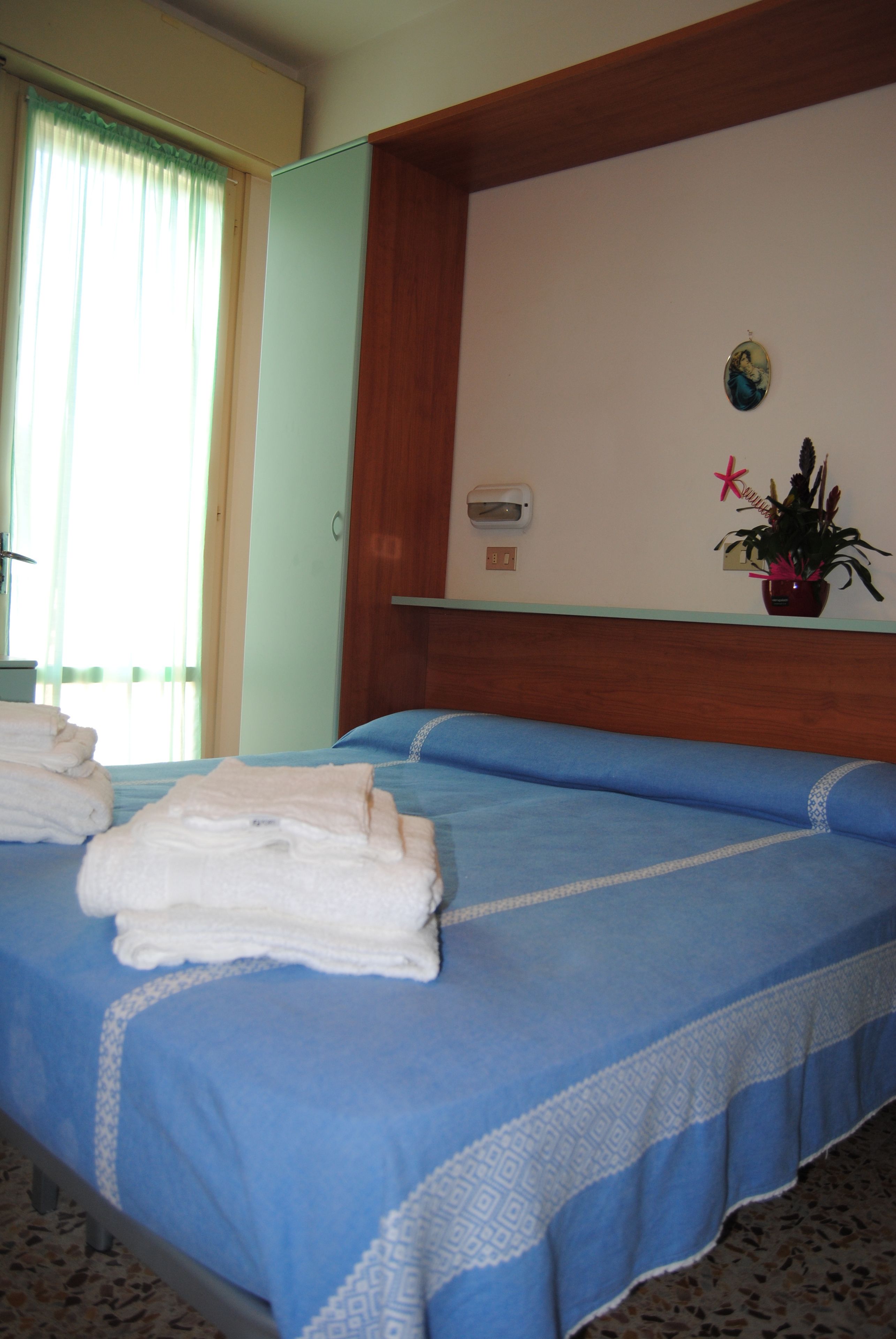A hotel room with a bed, a potted plant, and a wall-mounted shelf.