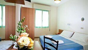 Una camera d'albergo con un letto, una scrivania con un vaso di fiori e una finestra con tende.