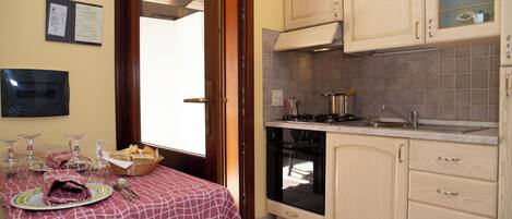 A kitchen with wooden cabinets, a stove, and a sink. There is a dining table with a tablecloth and cutlery.