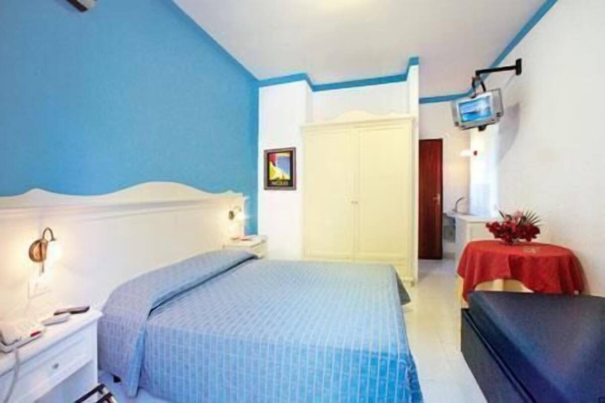 A bedroom with a bed, bedside table, wardrobe, and a TV mounted on the wall.