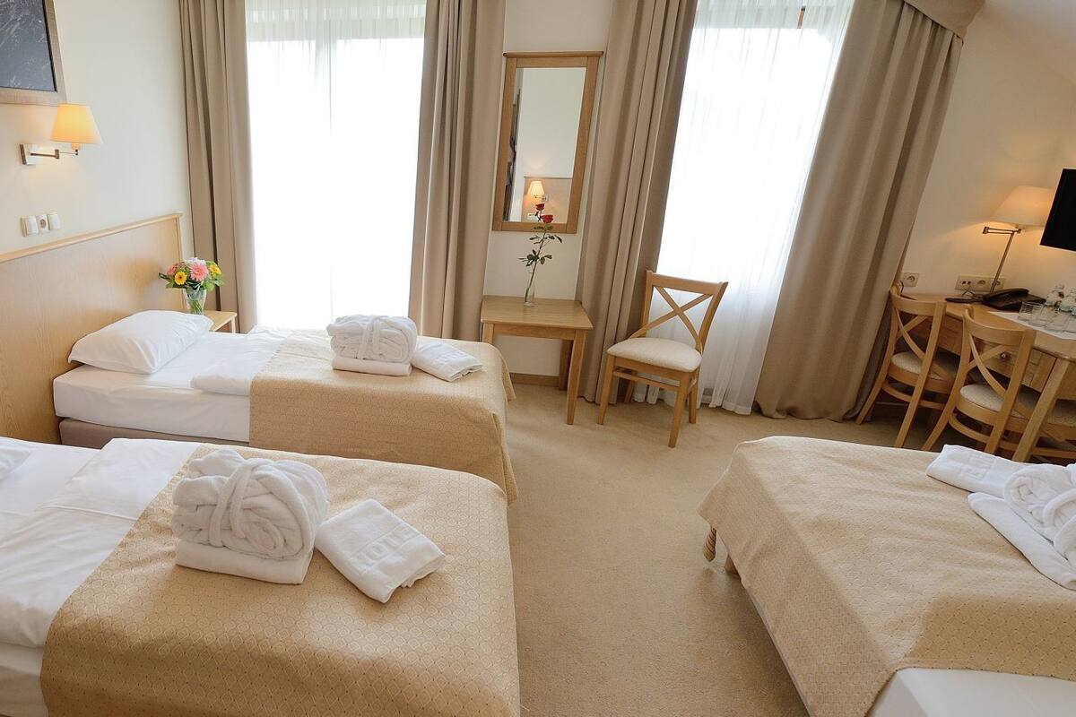 A hotel room with three single beds, a desk, a chair, and a TV.