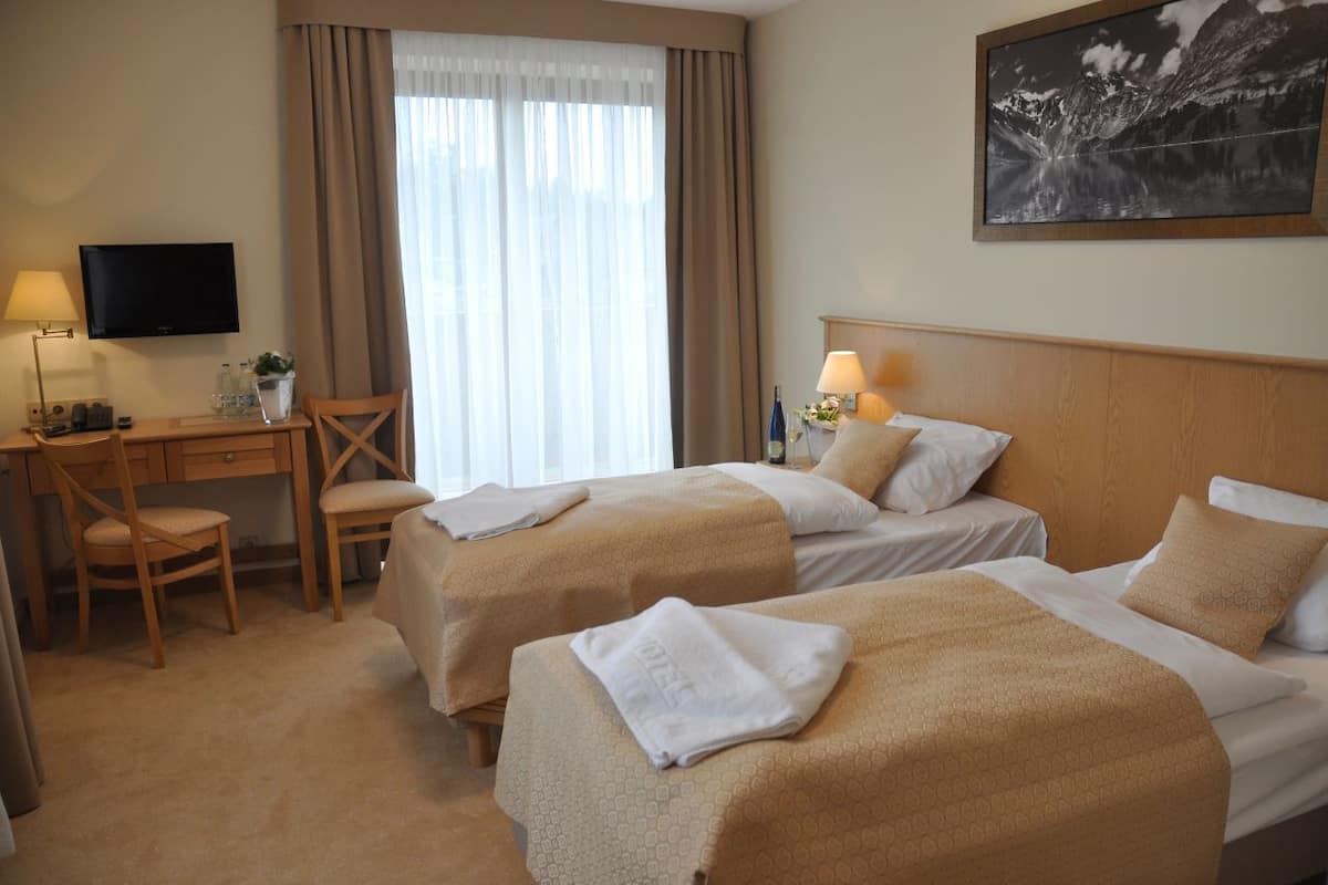 A hotel room with two beds, a desk, a chair, a TV, and a window with curtains.