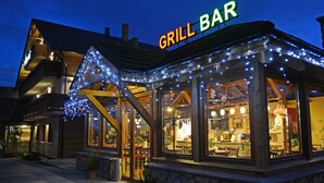 En restaurant med et 'GRILL BAR' skilt, med et overdækket udendørs areal, hvor der er tændt lyskæder, og en facade af natursten.