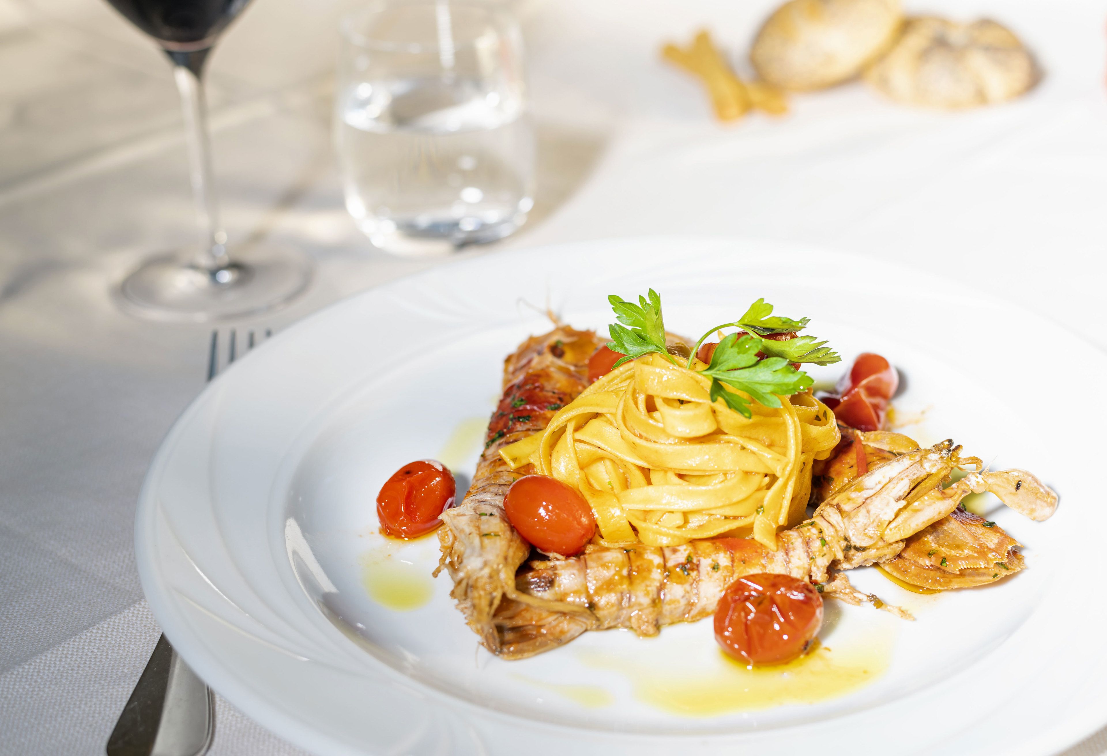 Un plato de pasta con un filete de pescado, tomates cherry y una guarnición sobre un plato blanco.