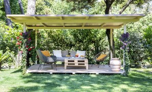 An outdoor patio with a wooden bench, two wicker chairs, and a table with drinks. - Hotel Andreaneri (Pietrasanta)