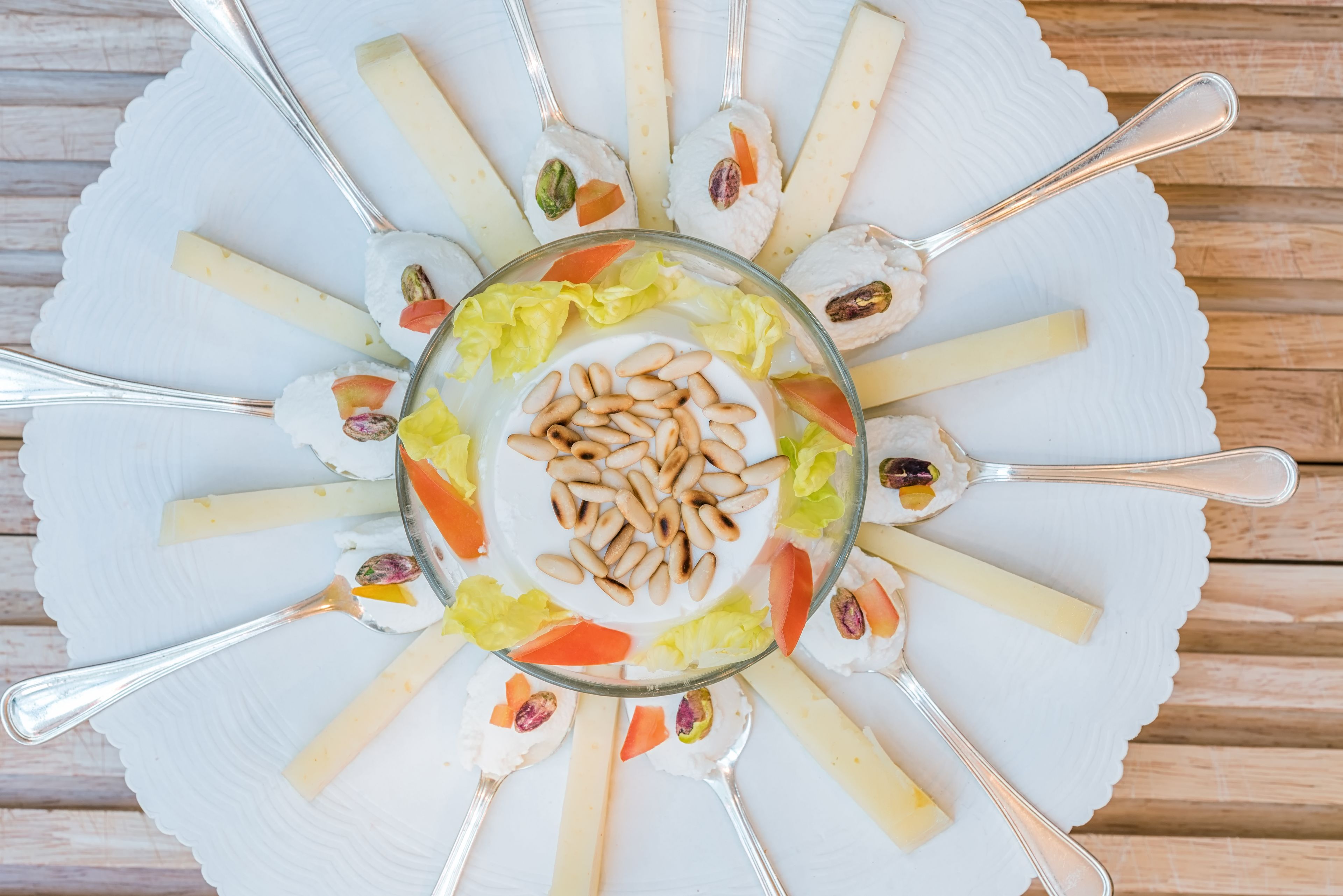 A white plate with various cheeses and nuts arranged in a circular pattern, with a central bowl of nuts and a spoon.