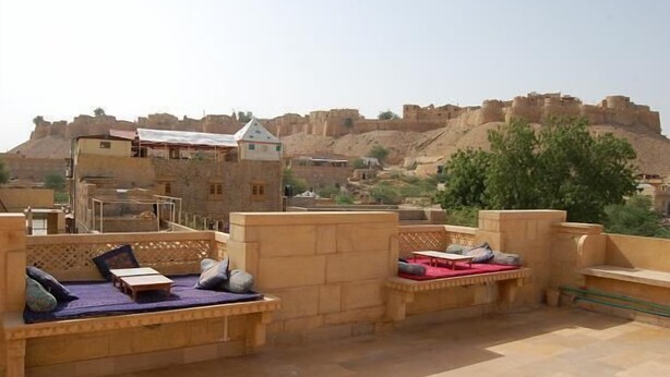 Eine Dachterrasse mit Sitzbereichen und Blick auf eine historische Festung, unter blauem Himmel.