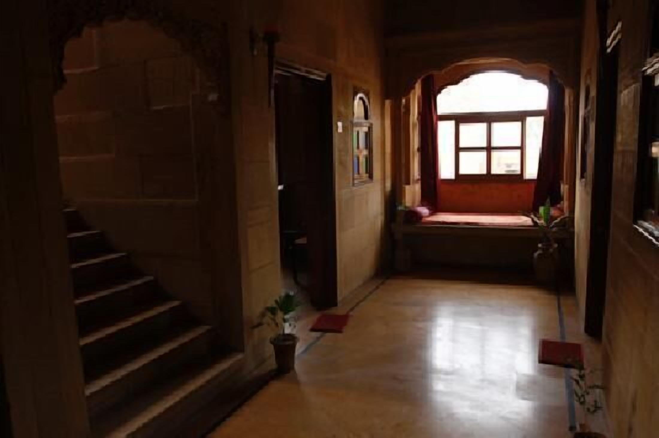 A corridor with a staircase on the left, a window with a view on the right, and a door at the end.