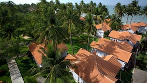 Ein Küstenresort mit mehreren Gebäuden und roten Ziegeldächern, umgeben von üppigen Palmen und Blick aufs Meer.