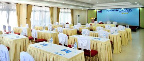 Une salle de conférence avec des tables préparées pour une réunion, comprenant des bouteilles d’eau, des documents et des chaises recouvertes de housses blanches.