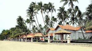 Ein Strandhotel mit strohgedeckten Gebäuden, Palmen und einem Sandstrand.