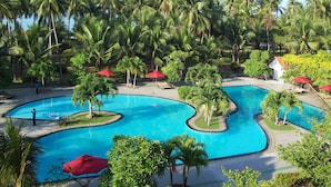 Ein Resort mit mehreren Schwimmbecken, umgeben von Palmen und roten Sonnenschirmen.