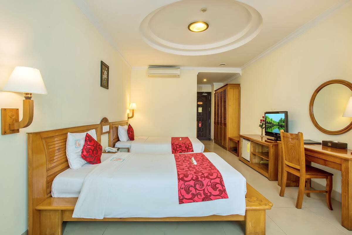 A hotel room with two beds, a desk, a chair, a TV, and a mirror.