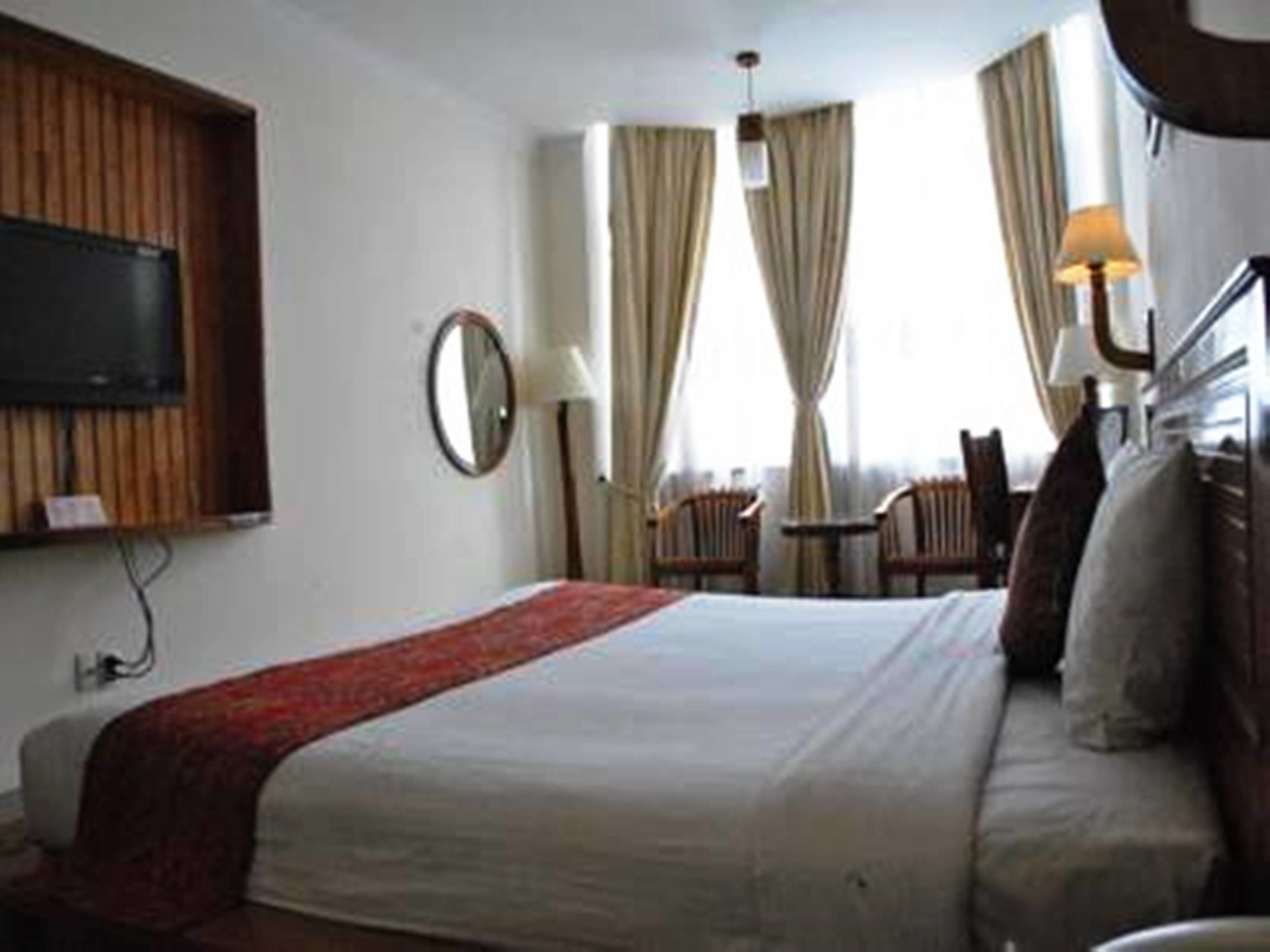 A hotel room with a bed, a TV mounted on the wall, a desk, and a chair.