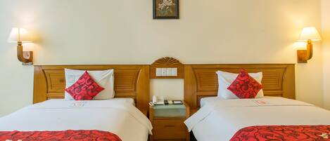 A hotel room with two beds, each with red and white bedding, a wooden headboard, bedside lamps, a nightstand with a phone, and a framed picture on the wall.