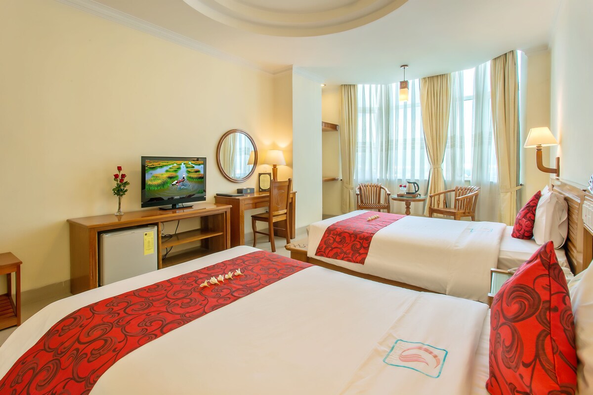 A hotel room with two beds, a desk, a television, and a chair.