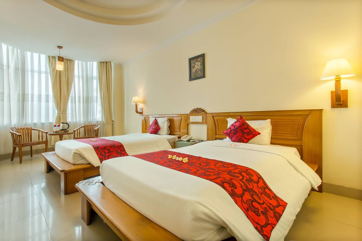 A hotel room with two beds, a desk, chairs, and a large window with curtains.