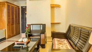 A compact hotel room with a wooden wardrobe, a small table with a vase and a tray, a sofa, and a bed with a patterned cover. - Golden Sea Hotel (Da Nang)