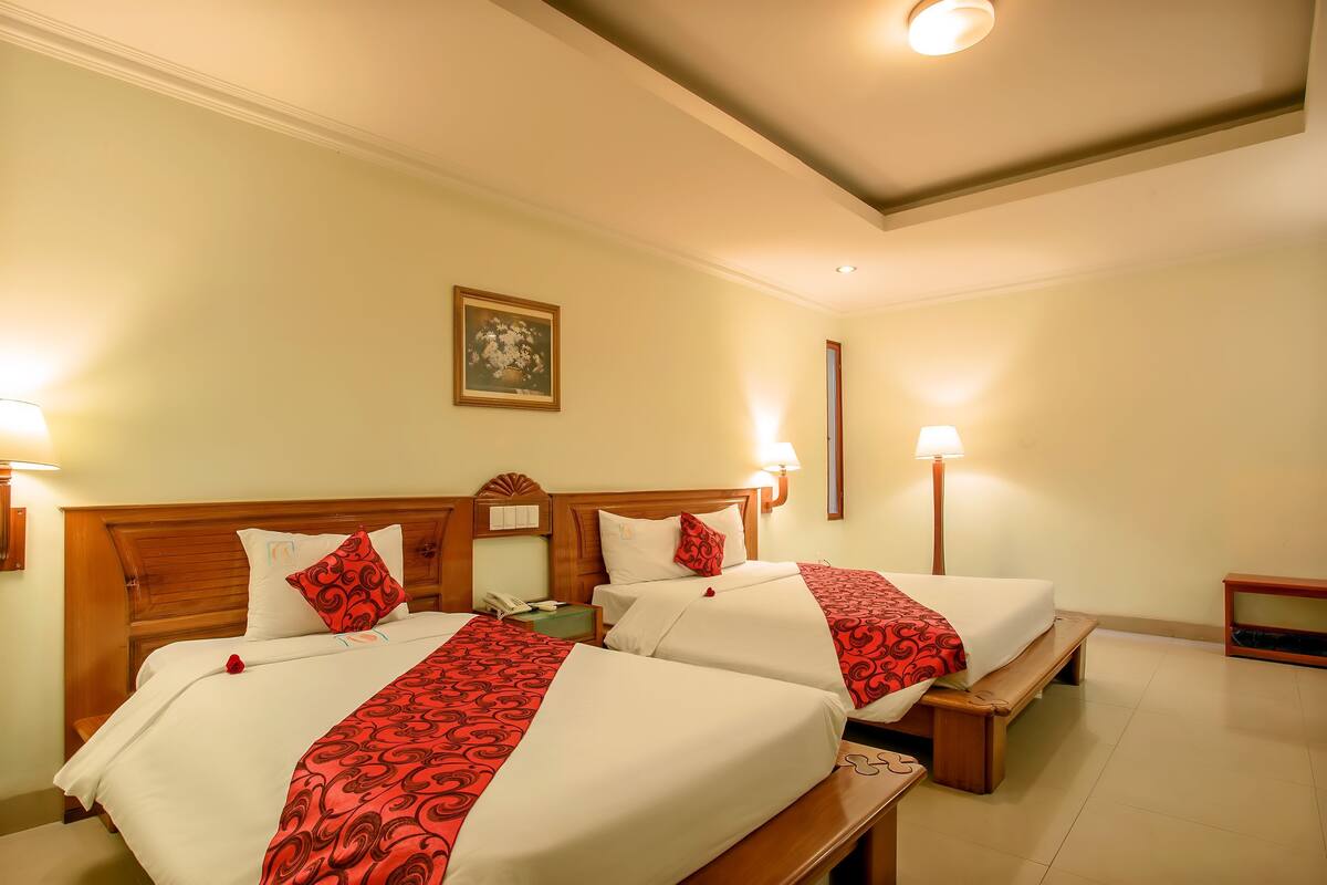 A hotel room with two beds, wooden headboards, bedside lamps, a nightstand, and a framed picture on the wall.