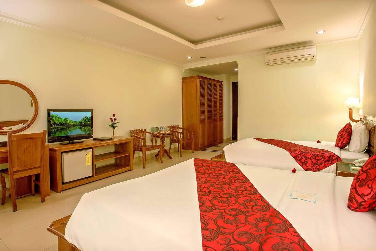 A hotel room with two beds, a TV, a desk with a computer, a small fridge, and a wardrobe.